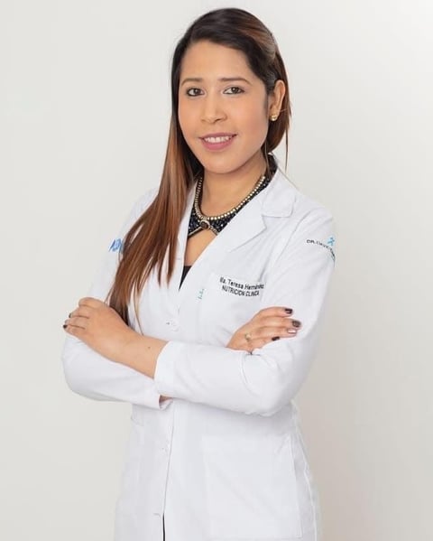 Female healthcare professional in white lab coat with arms crossed, smiling at camera against white background