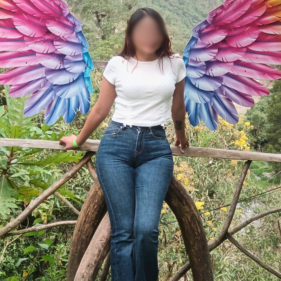 Person wearing white t-shirt and jeans with large colorful gradient wings standing on wooden railing in nature