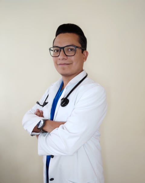 Male doctor wearing glasses and white coat with stethoscope, arms crossed, smiling at camera