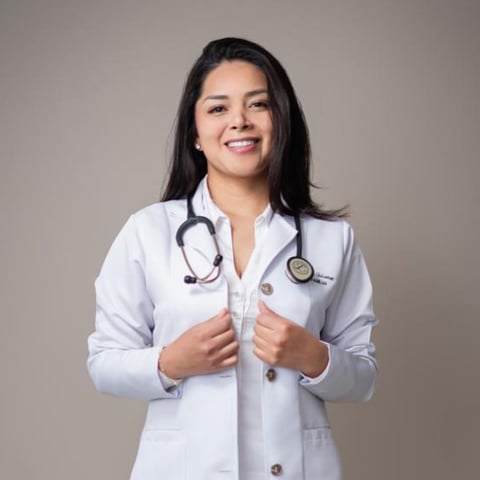 Female doctor in white coat and stethoscope smiling at camera against gray background